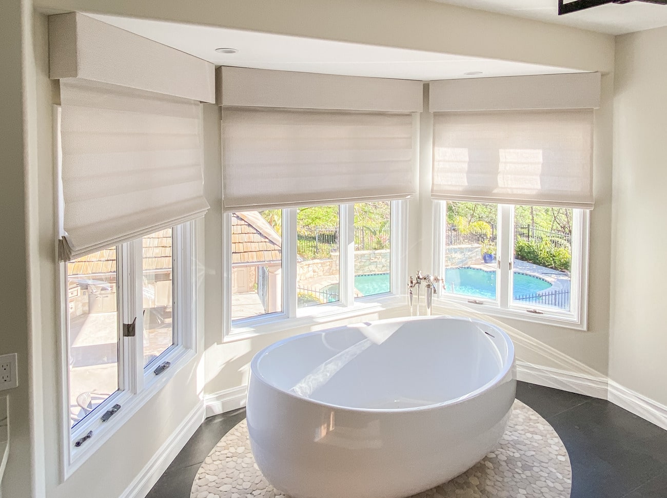Free-standing bathrub in front of bay windows with half-drawn roller shades